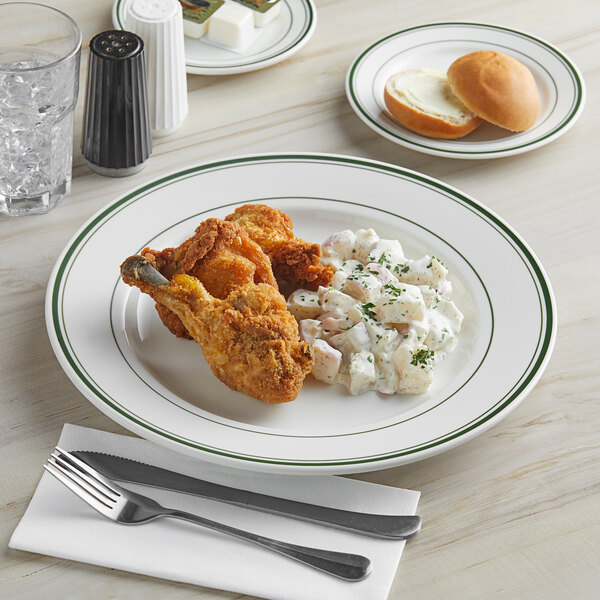 A Tuxton Green Bay ivory china plate with green bands holding fried chicken and mashed potatoes.