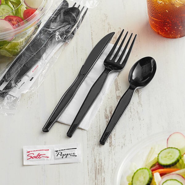 A black fork, knife, and spoon wrapped in a napkin.