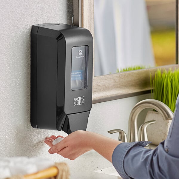 A woman using a Pacific Blue Ultra manual hand sanitizer dispenser on a counter.