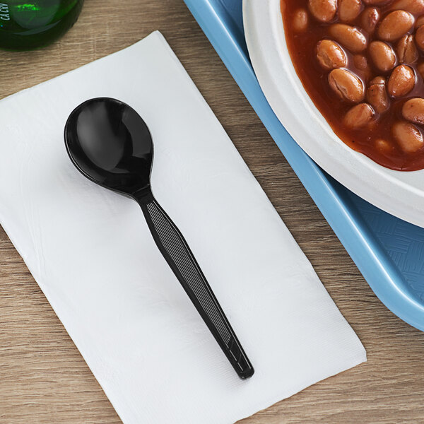 A black Dixie heavy weight polystyrene spoon next to a bowl of beans with sauce.
