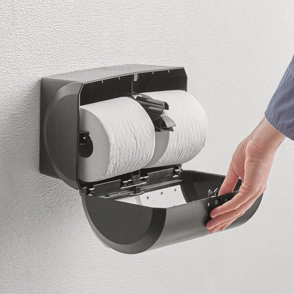 A hand using a Compact by GP Pro double coreless roll toilet paper dispenser.