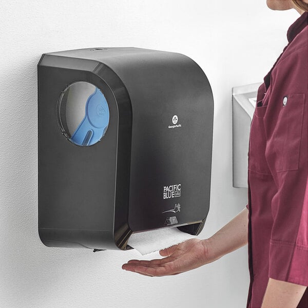 A woman using a Pacific Blue Ultra automatic paper towel dispenser in a hospital cafeteria.