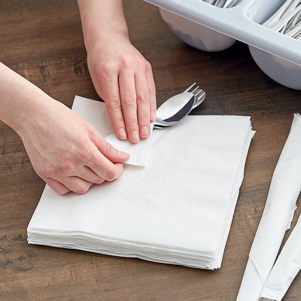 A person's hands cutting a white Dixie paper dinner napkin with a fork and spoon.