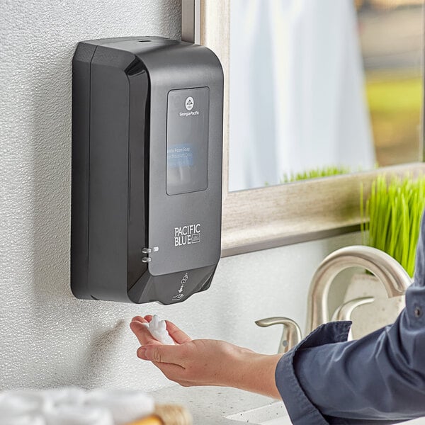 A woman using a Pacific Blue Ultra touchless hand sanitizer dispenser on a counter.