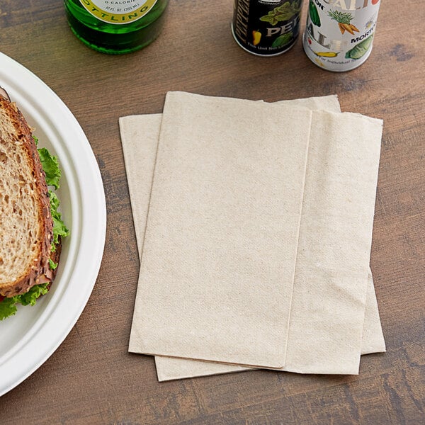 A sandwich on a plate with a brown Dixie napkin next to two cans of beer.