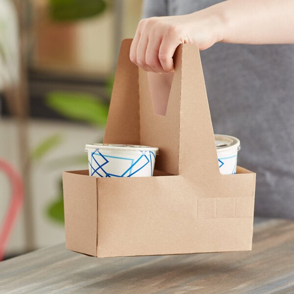A hand holding a brown bag with a Choice drink carrier filled with two cups.