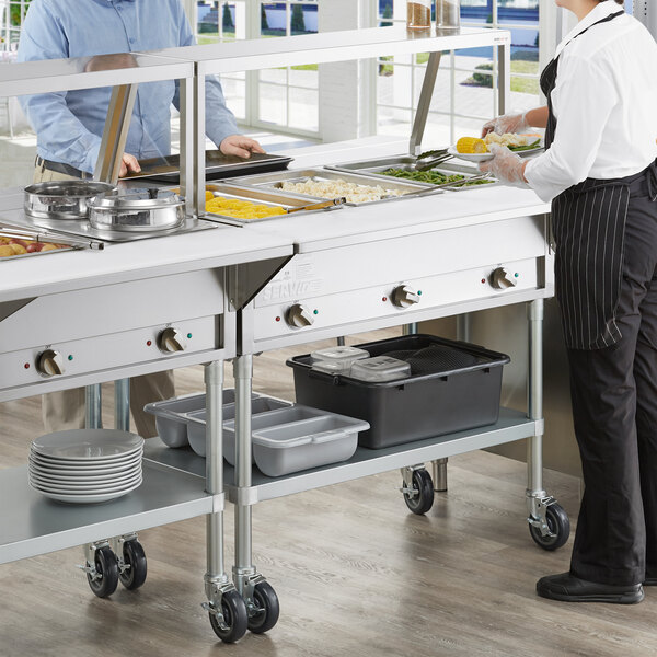 A man and woman using a ServIt steam table in a cafeteria.