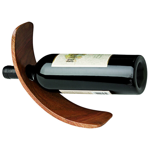 A Franmara wood curved wine bottle stand holding a bottle of wine on a table.