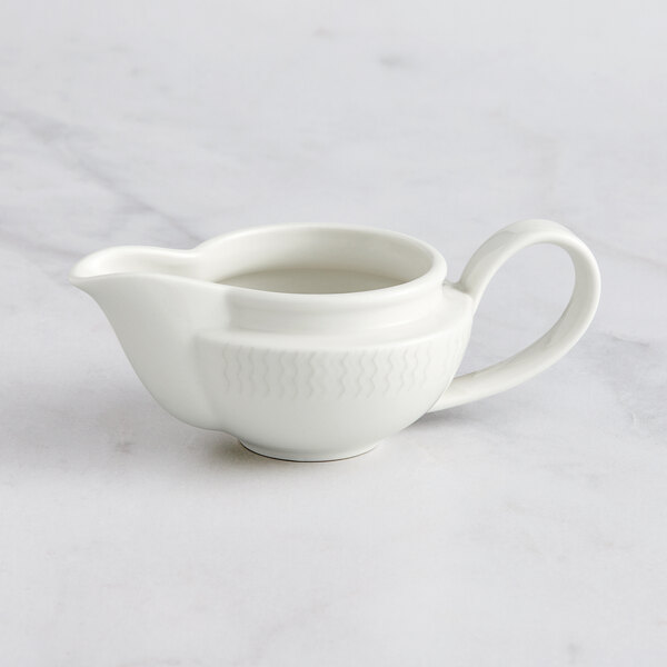 A RAK Porcelain ivory gravy boat with an embossed pattern and a handle on a white surface.