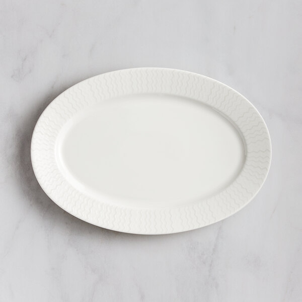 A RAK Porcelain ivory oval platter with wavy lines on a marble surface.