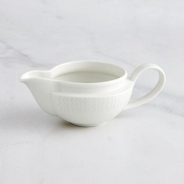 A white RAK Porcelain gravy boat with an embossed design and a handle.