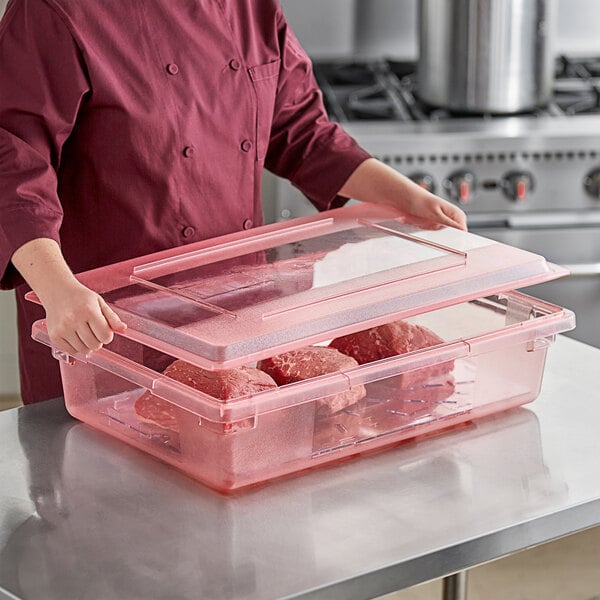 A woman in a red chef's uniform holding a Carlisle red food storage container with a lid.