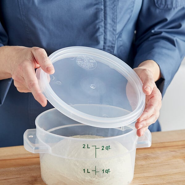 A woman holding a Vigor translucent round polypropylene food storage container with a lid.