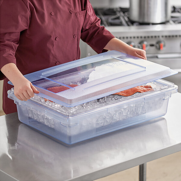A woman in a chef's uniform holding a Carlisle blue plastic food storage box with a lid.