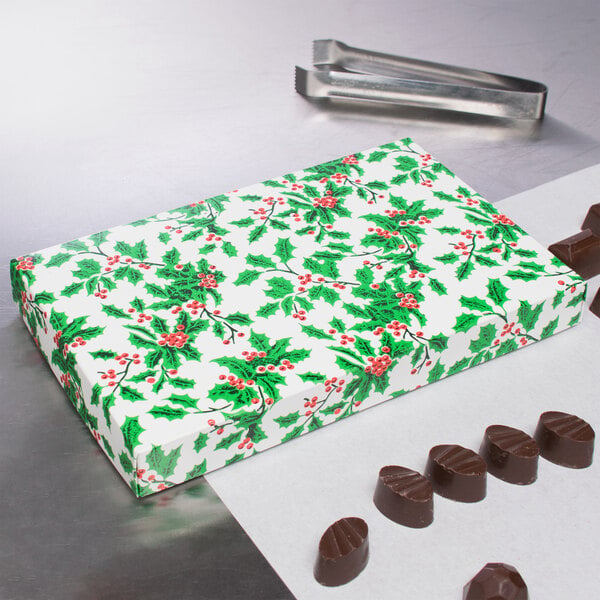 A 2-piece holly patterned candy box next to chocolates.