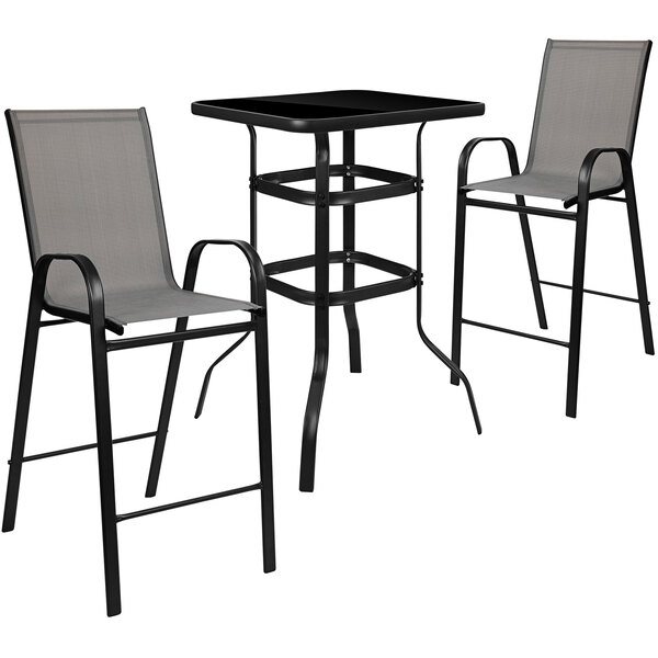 An outdoor bar table with glass top and two grey chairs with black frames.