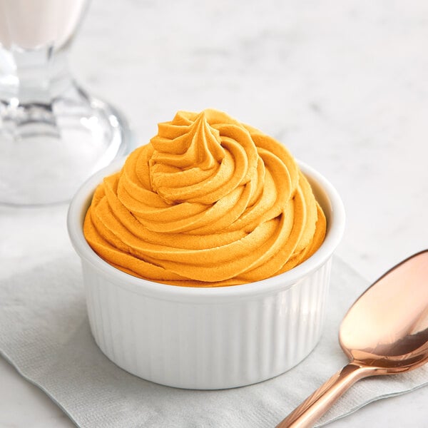 A bowl of orange soft serve with a spoon on a table.