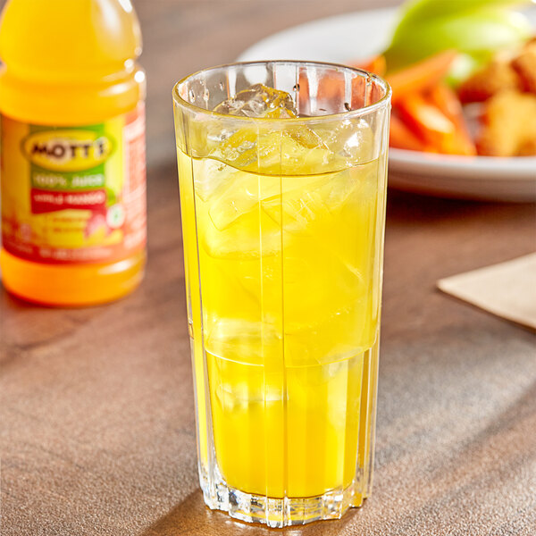 A glass of Mott's Apple Mango Juice with ice on a table with a plate of food.