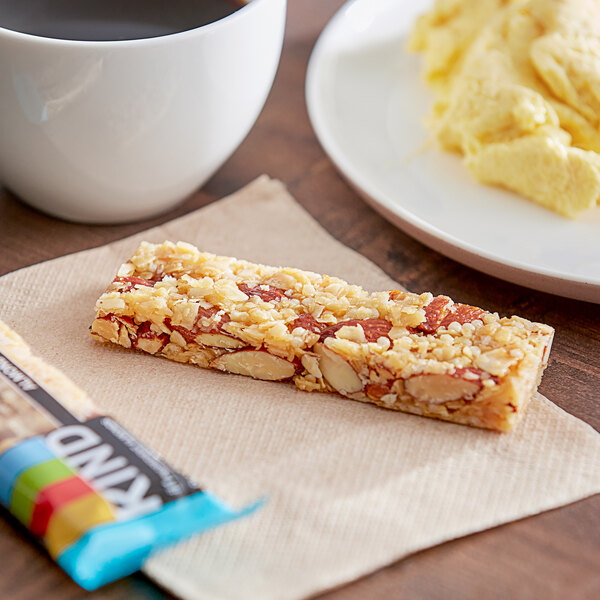 A KIND Almond & Coconut Bar on a napkin next to a plate of food.