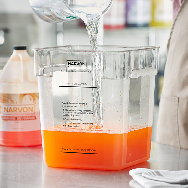 A person pouring orange juice into a Narvon slushy mix container on a counter.