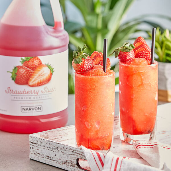 A couple glasses of red strawberry slushy with a pitcher of Narvon Strawberry Slushy Concentrate.