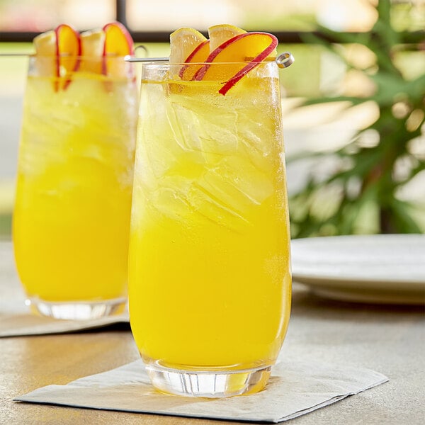 Two glasses of yellow liquid with slices of fruit on top.