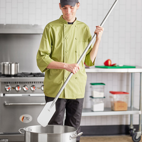 A man in a chef's uniform using a Fourt&#233; stainless steel paddle to stir a large pot on a stove.