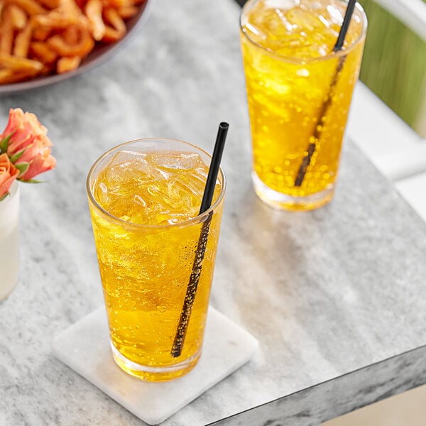 Two glasses of orange soda with a straw on a marble table.