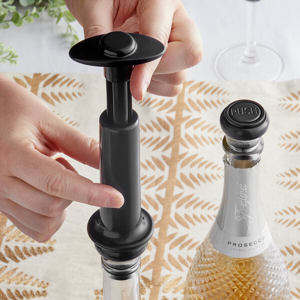 A hand holding a Franmara VinoVac black wine saver vacuum pump next to a bottle of wine.