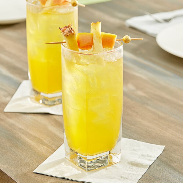 Two glasses of yellow pineapple papaya juice with fruit on a wooden table.