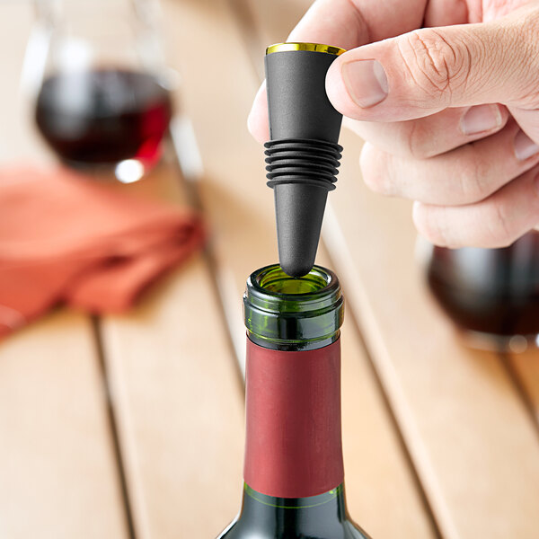 A person's hand using a Franmara gold and black bottle stopper to seal a bottle of wine.