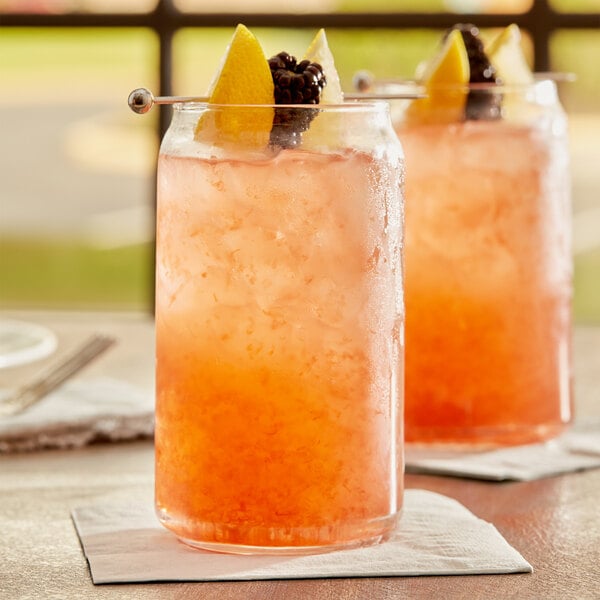 A glass of pink Pure Craft Blackberry Lemonade with orange and lemon slices on a table.