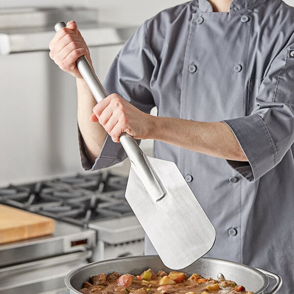 A person using a Fourté stainless steel paddle to cook food in a pan.