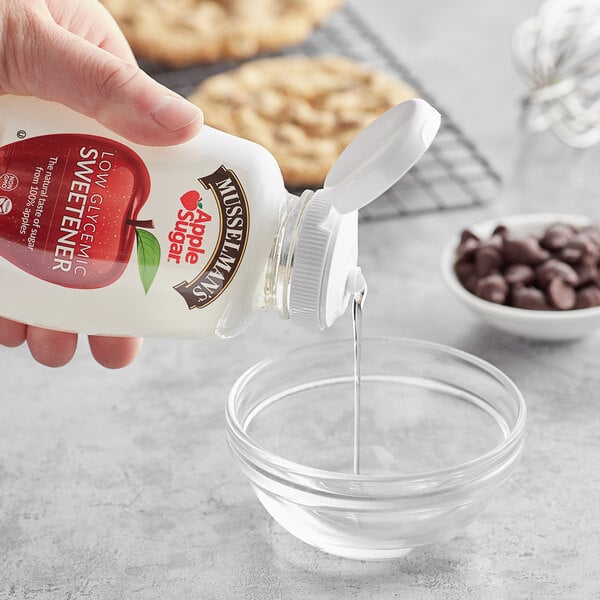 A hand pouring Musselman's Low Glycemic Apple Sugar Sweetener into a clear bowl.