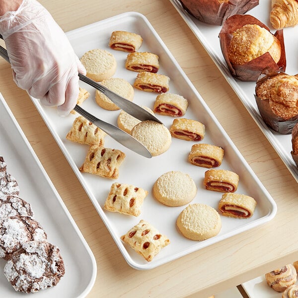 A hand in a plastic glove using tongs to serve pastries on a white MFG Tray.