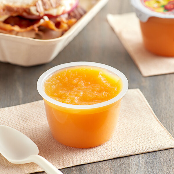 A close-up of a Musselman's Lite Mango Orange Applesauce cup on a napkin with a spoon.