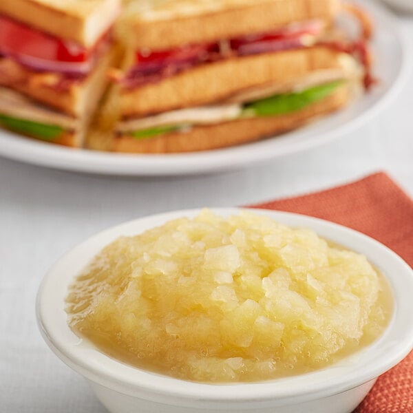 A bowl of Musselman's apple sauce on a table with a plate of sandwiches.
