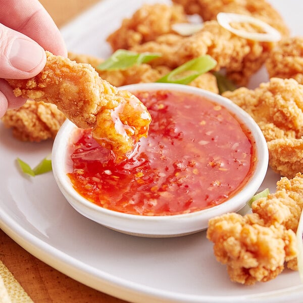 A hand dipping a piece of fried chicken into Mae Ploy Sweet Chili Sauce.