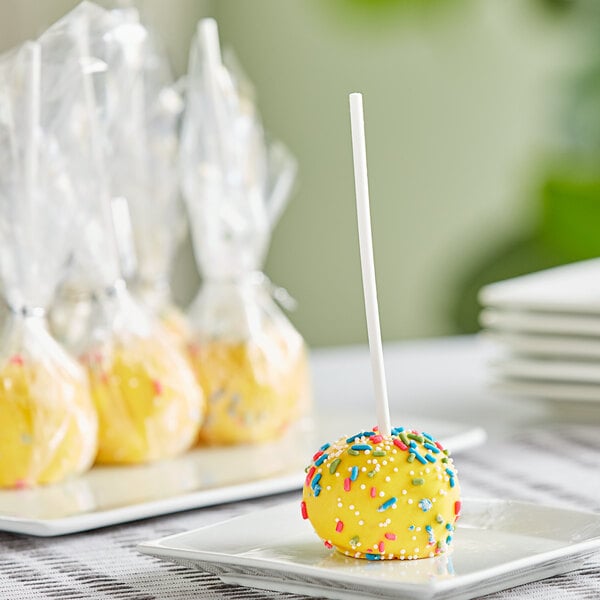 A yellow Chalet Desserts lemon cake pop with sprinkles on a white plate.