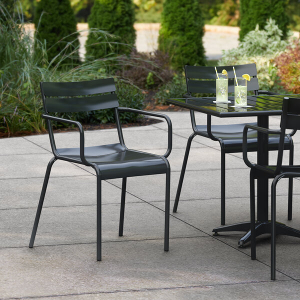A Lancaster Table & Seating black powder coated aluminum outdoor arm chair at a table with drinks on a patio.