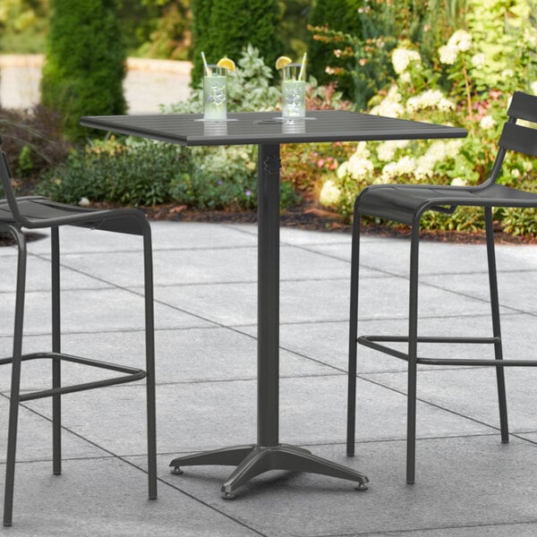 A Lancaster Table & Seating black bar height outdoor table with two black chairs on a patio.