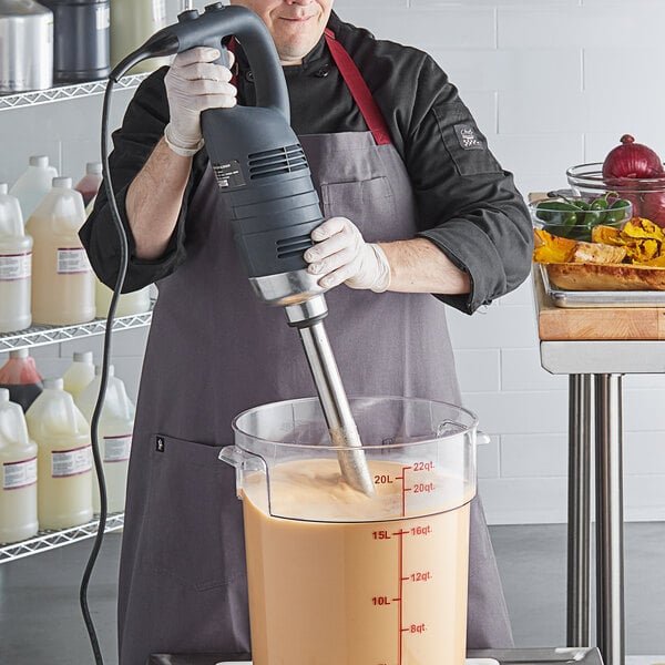 A person using an AvaMix heavy-duty immersion blender to mix liquid in a bowl.