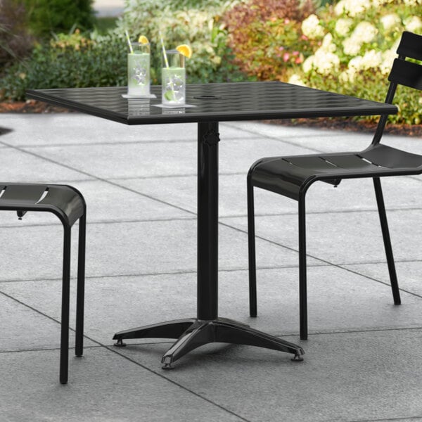 A black Lancaster Table & Seating outdoor table with chairs on a patio.