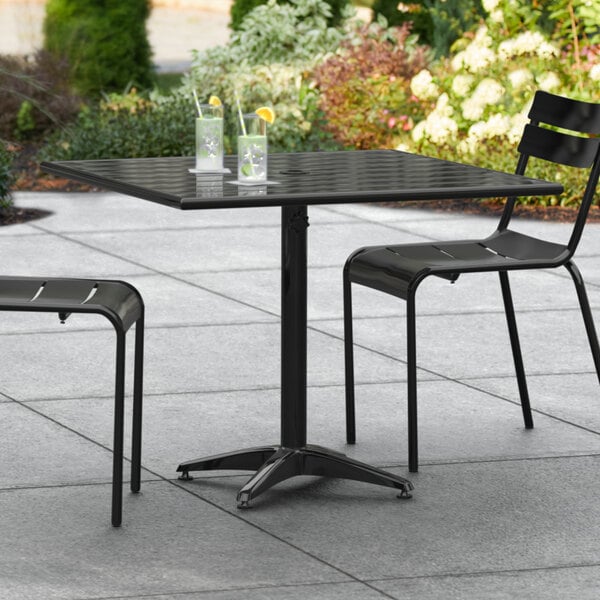 A black Lancaster Table & Seating outdoor dining table with chairs on a patio.