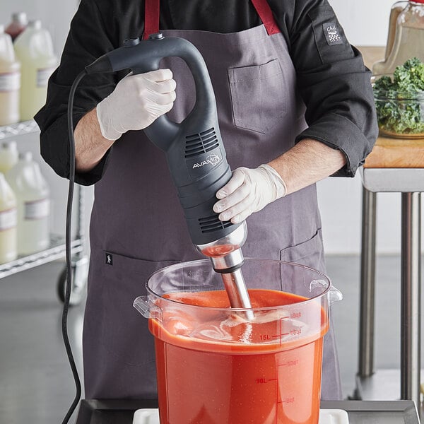 A man in a chef's uniform using an AvaMix heavy-duty immersion blender to mix a red liquid.