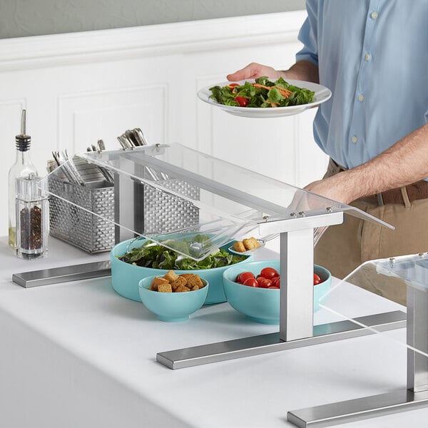 A man serving himself salad at a table with a Pass-Through Countertop Sneeze Guard.