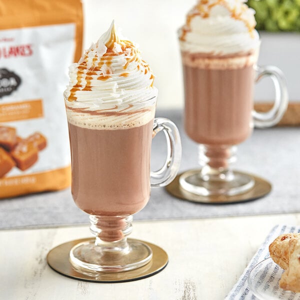 Two glasses of Land O Lakes Salted Caramel and Chocolate hot chocolate with whipped cream and caramel sauce.