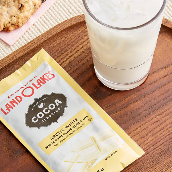 A glass of milk and a packet of Land O Lakes Arctic White Chocolate Cocoa mix on a wooden tray.
