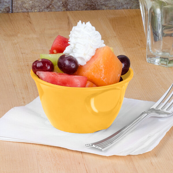 A yellow Thunder Group melamine bowl filled with fruit and whipped cream with a fork.