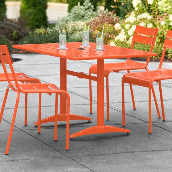 A Lancaster Table & Seating orange powder-coated aluminum table with chairs on a patio.